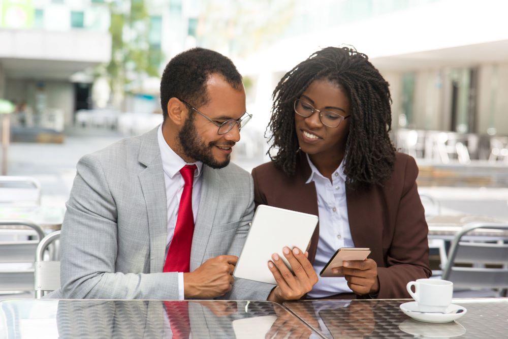 cheerful-coworkers-looking-each-other-gadgets-screen