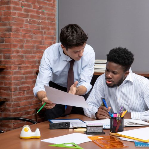 front-view-two-busy-businessmen-formal-wear-one-them-showing-paper-another-one-office front-view-two-busy-businessmen-formal-wear-one-them-showing-paper-another-one-office